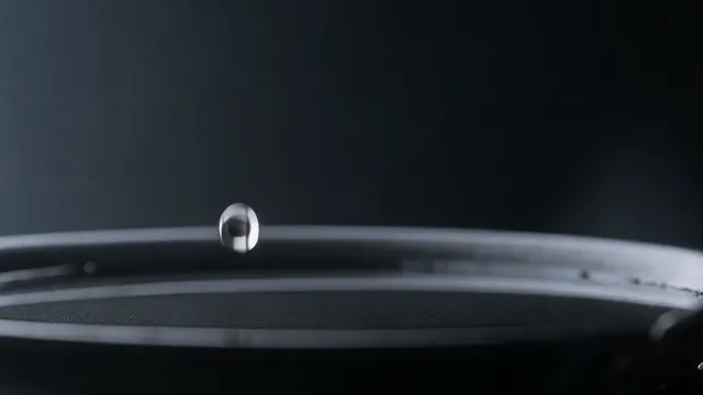 Wan 2.7 — The camera holds still and level with the surface. A single drop falls into a shallow black dish